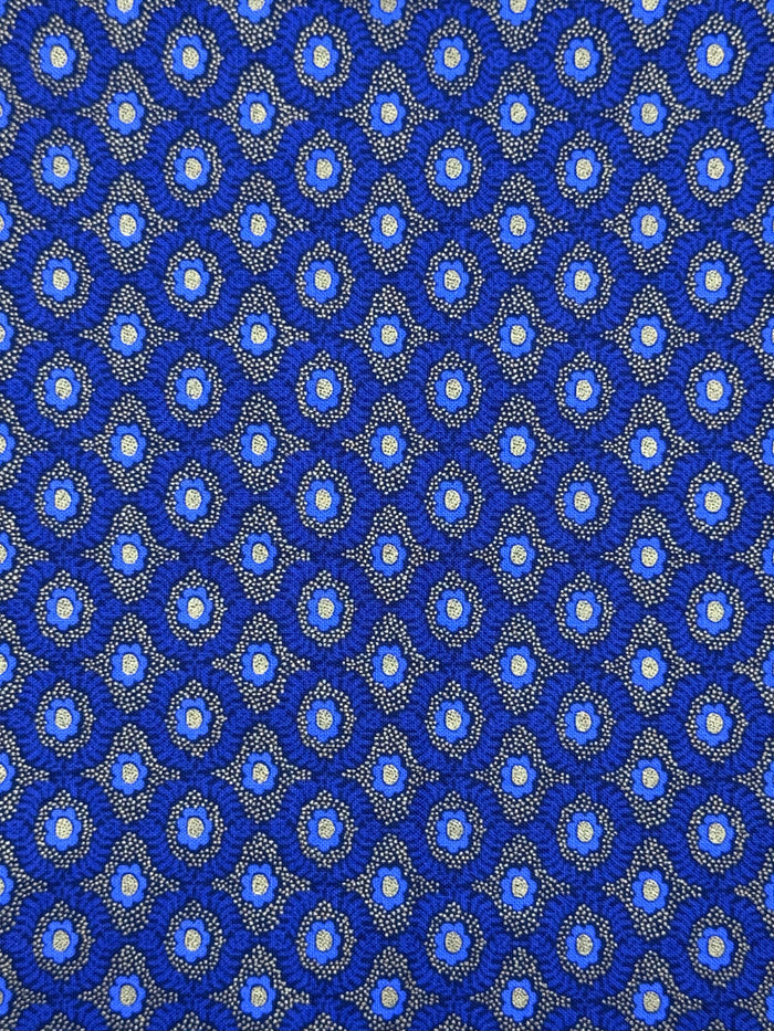 A close-up of a repeating blue patterned fabric or material with small circular motifs and fine dotted details in white, light blue, and gray.