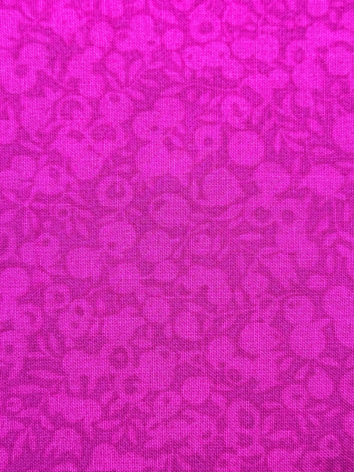 A close-up of a bright magenta pink fabric with a tonal floral pattern.