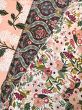 A close-up of a folded fabric showing two different floral and paisley patterns. One side features a dusty pink background with white floral motifs, while the other side displays a cream base with a dense print of pink, red, and green flowers and leaves, accented by a dark maroon paisley border.