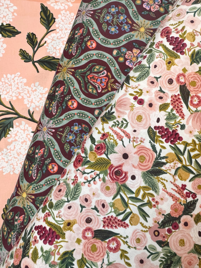 A close-up of a folded fabric showing two different floral and paisley patterns. One side features a dusty pink background with white floral motifs, while the other side displays a cream base with a dense print of pink, red, and green flowers and leaves, accented by a dark maroon paisley border.
