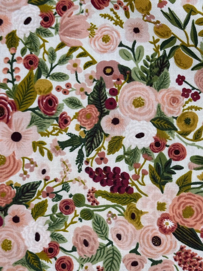 A close-up of a floral fabric pattern featuring pink, white, and burgundy flowers with green and olive leaves on a white background.