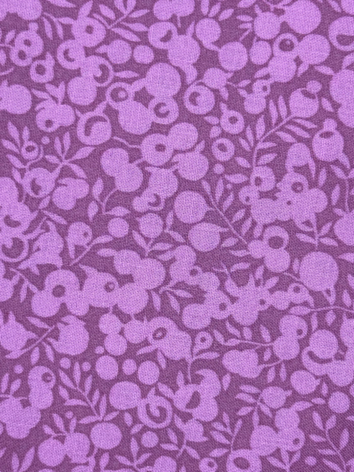 A close-up of a purple fabric with a repeating floral pattern in a slightly lighter lavender shade.