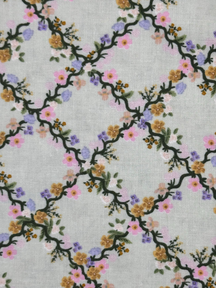 A close-up of a fabric pattern featuring a trellis design with dark green vines and small flowers in pink, purple, yellow, and orange on a light gray background.