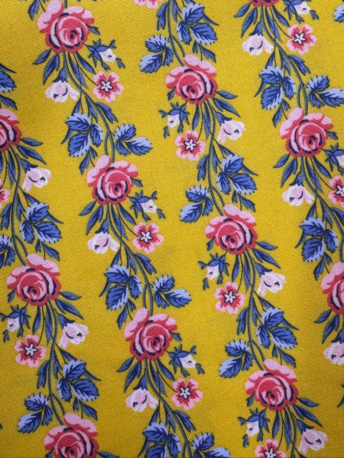 Floral fabric with pink and blue flowers on a yellow background, placed on a wooden surface.