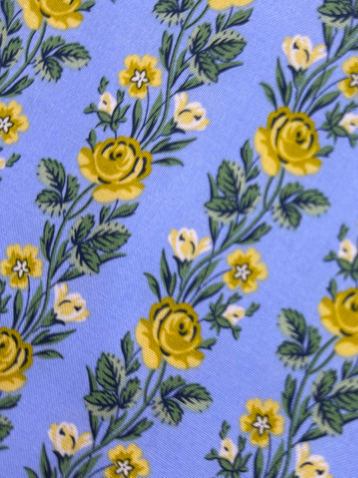 Floral patterned fabric with yellow flowers on a blue background, placed on a wooden surface.