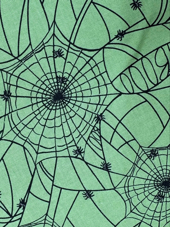 Green fabric with black spider web pattern on a wooden surface