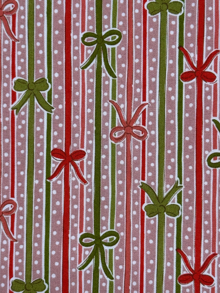 A close-up of a patterned fabric featuring vertical red and green stripes with white polka dots, interspersed with green and red ribbon-bow motifs.