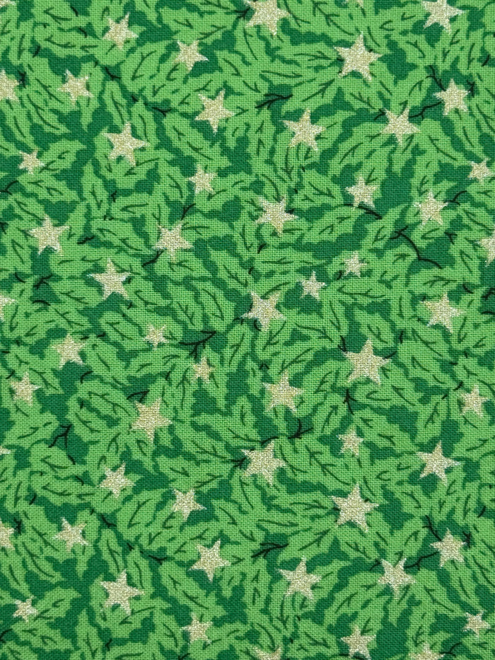 A close-up of a green patterned fabric featuring a repeating design of light green pine branches and cream-colored five-pointed stars.