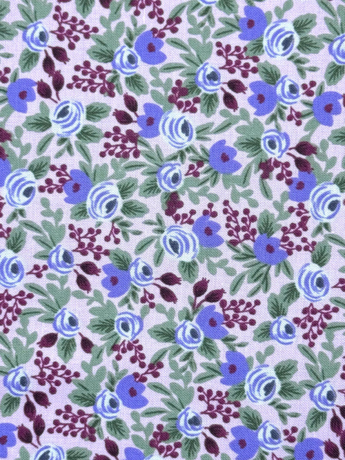 A close-up of a floral fabric pattern featuring blue and purple flowers with green leaves on a pale lavender background.