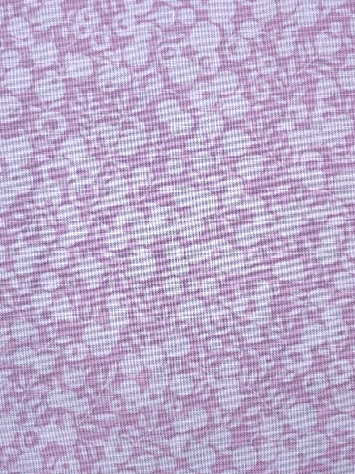 A close-up of pink fabric with a repeating white floral and berry pattern.