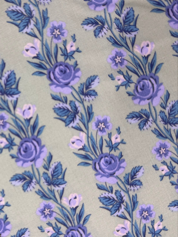 Floral fabric with purple flowers on a green background, placed on a wooden surface.