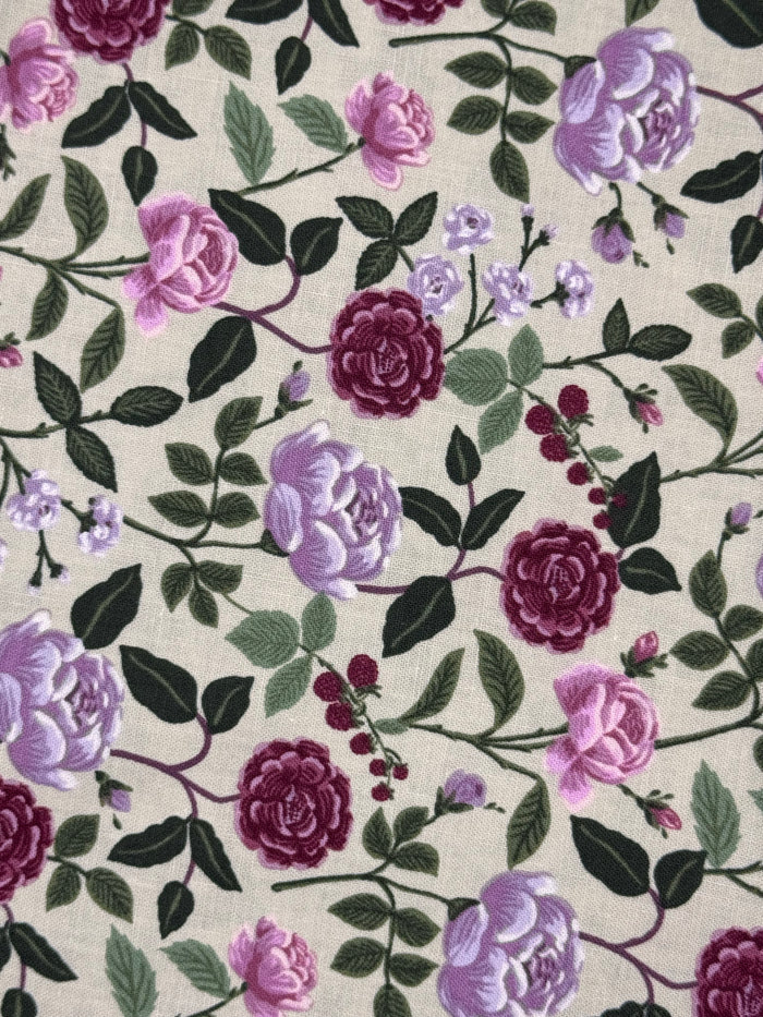 A close-up of a floral fabric pattern featuring large pink and purple roses, dark green leaves, and small berry clusters on a light beige background.