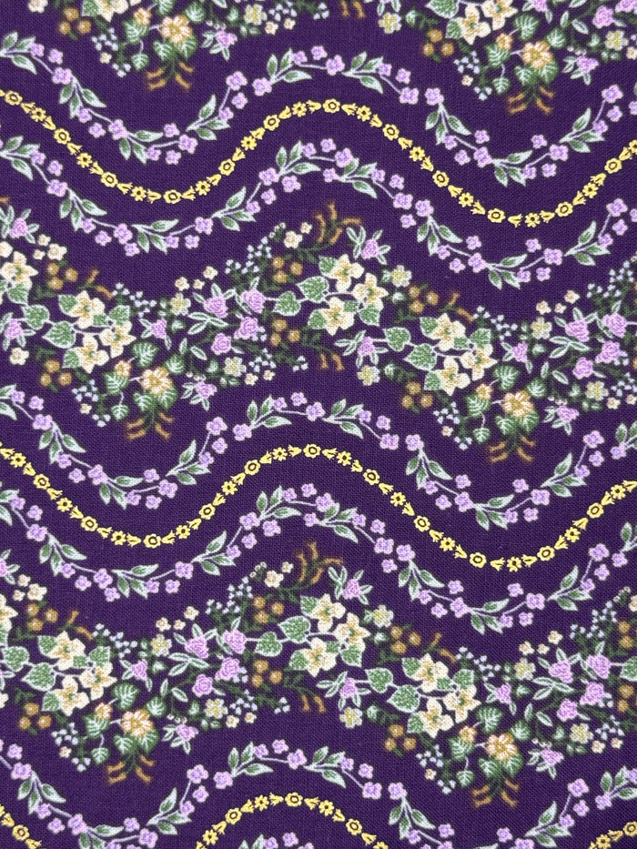 A close-up of a repeating floral pattern on fabric or wallpaper, featuring wavy garlands of small purple, white, and yellow flowers with green leaves on a deep purple background.