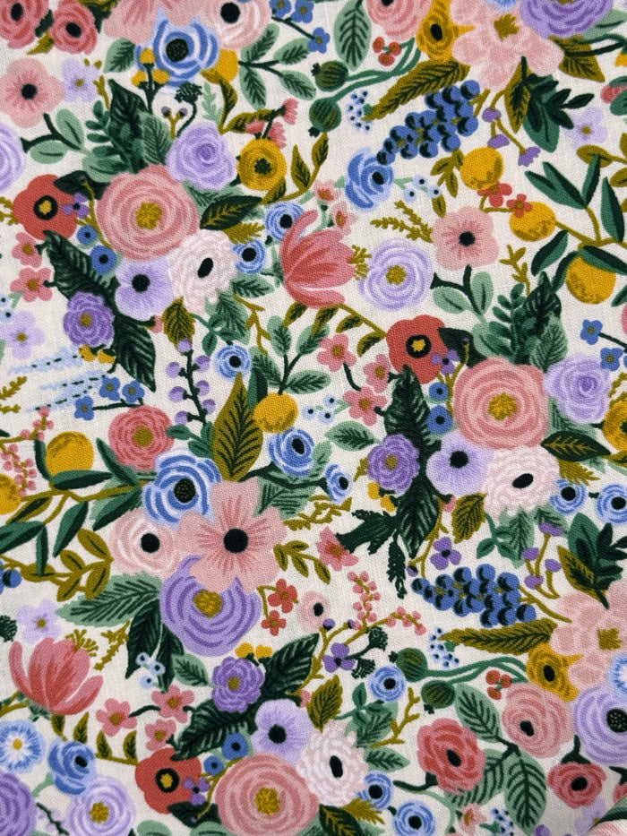 A close-up of a floral fabric pattern featuring pink, purple, blue, yellow, and green flowers and leaves on a white background.